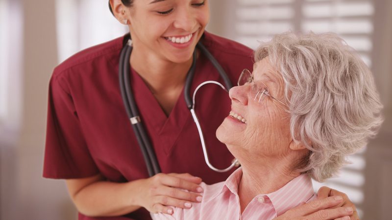 Female hospice nurse looking and smiling with senior woman.