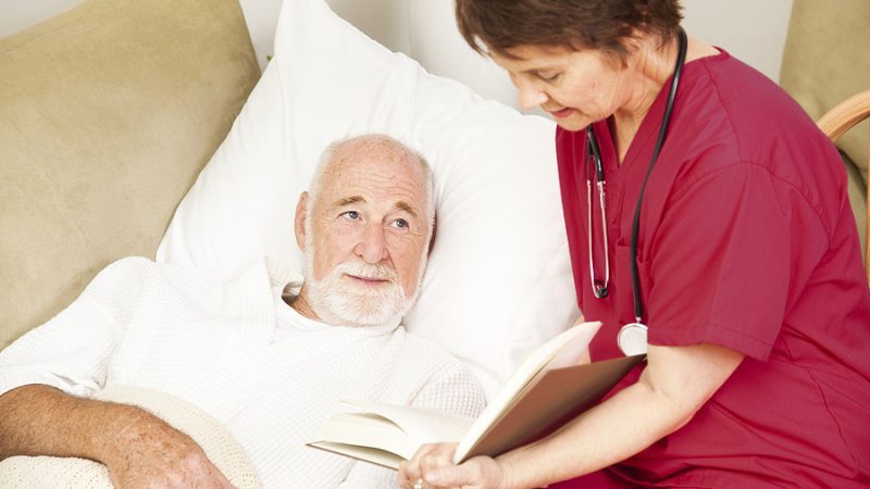 Friendly home caregiver reads to an elderly patient.