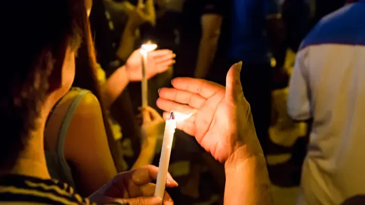A person holding a candle outside at night with their other hand placed in front of the flame.