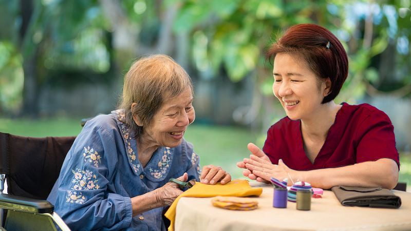 An elderly hospice patient does crafts at home with the help of a hospice nurse.