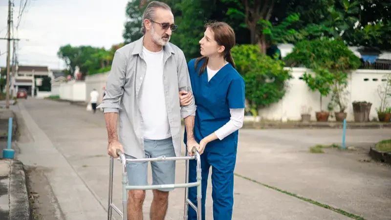 A nurse holding an elderly man's arm who is using a walker.